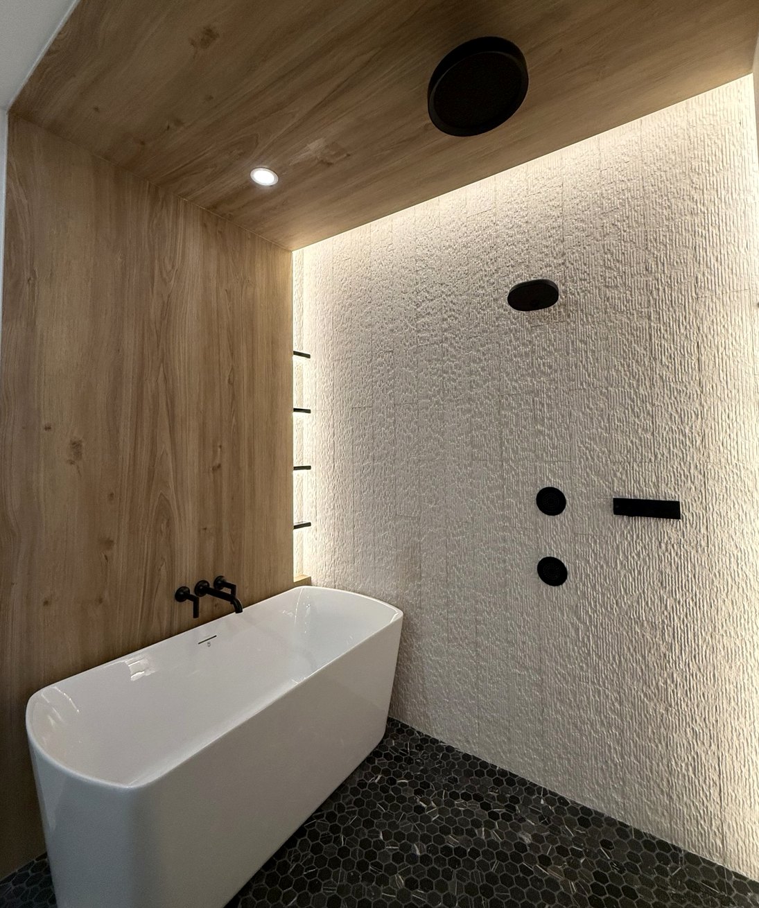 Finished freestanding white bathtub against textured wall with modern black plumbing fixtures